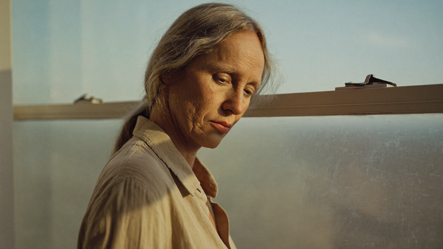 A woman at a window in early autumn morning light, bare skin without makeup