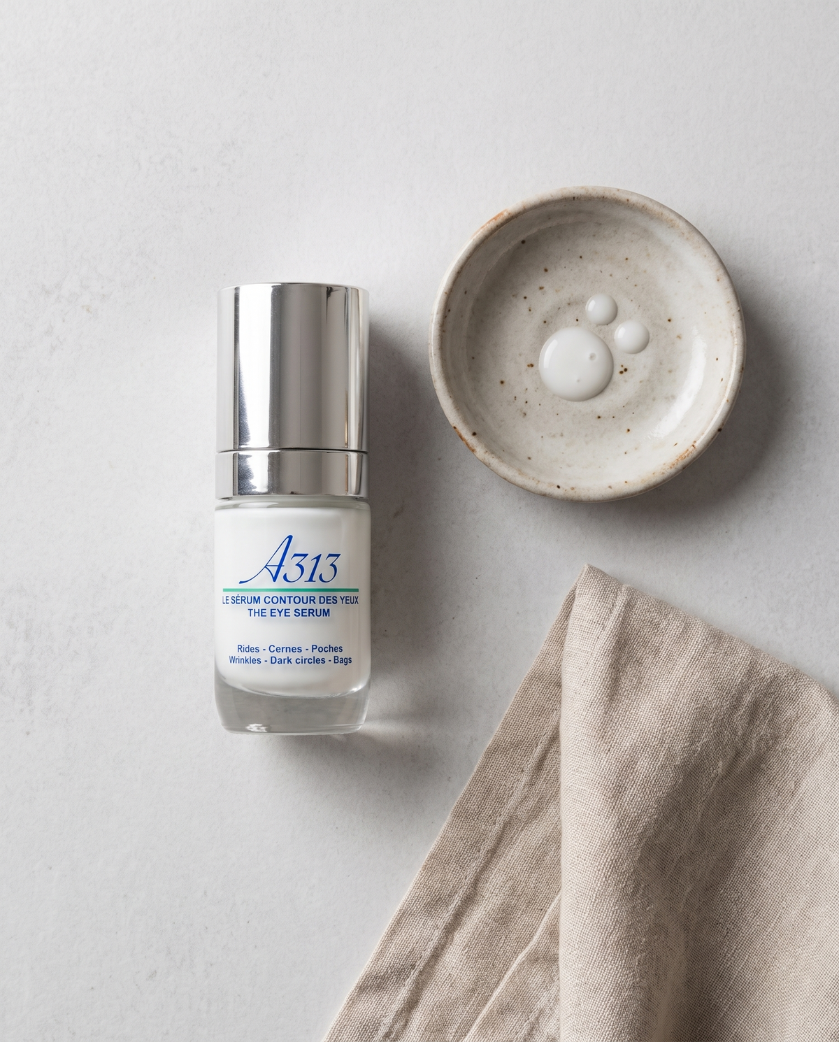 A313 Eye Serum bottle in an overhead flatlay beside a small ceramic dish and a folded linen cloth in soft daylight