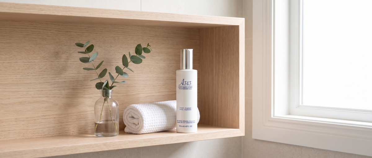 Flacon de lait corps A313 Lifting Body Milk posé sur une étagère de salle de bain en bois clair, près d'une serviette blanche roulée et d'un brin d'eucalyptus