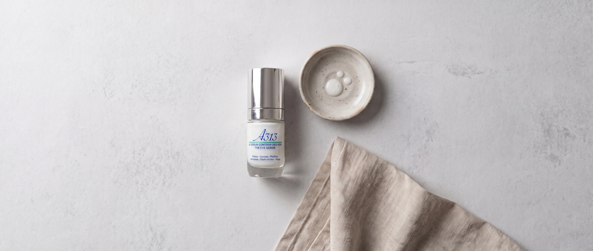 Flesje A313 Eye Serum van bovenaf gefotografeerd naast een klein keramisch schaaltje en een opgevouwen linnen doek in zacht daglicht